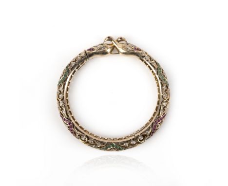 A gold, emerald, ruby and diamond bangle, the hinged openwork bangle designed as a pair of birds, their tails forming the bra