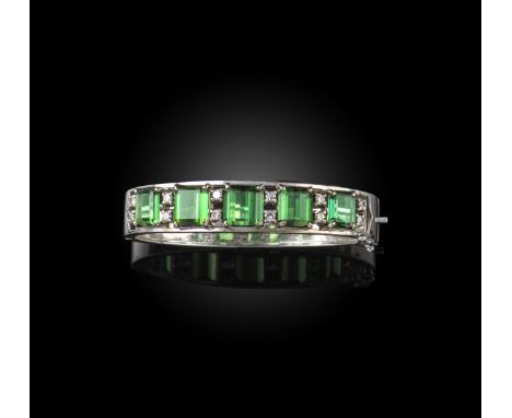 A tourmaline and diamond bangle, 1960s, the hinged bangle in white gold, set to the front with a graduated line of step-cut g