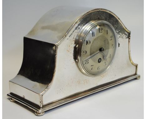 A George V silver plated mantel clock, plannished front, silver dial, black Arabic numerals, French 14 day movement, bun feet