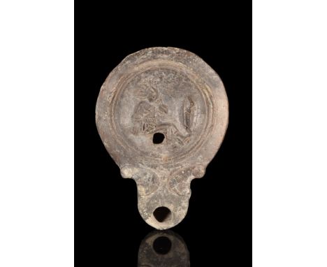 Ca. 100-300 AD. A mould-made terracotta oil lamp with concave discus bearing a relief image of a defeated gladiator facing ri