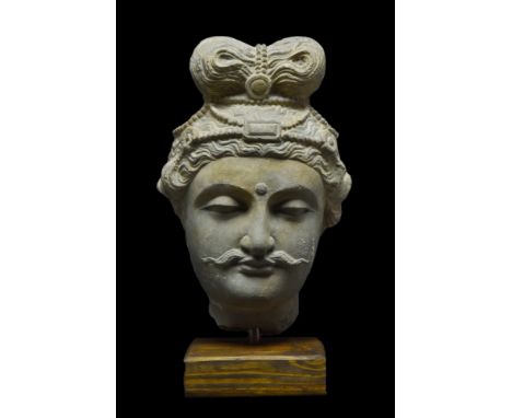 Ca. 100-300 AD. A schist stone head of a Buddha. He is depicted with wavey hair gathered up in a topknot above a headband. Hi