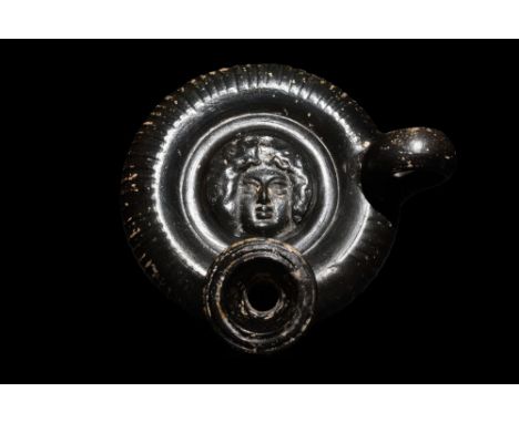 Ca. 360-320 BC. A black-glazed terracotta guttos (oil-lamp filler) with a spool-shaped foot, a wheel-shaped body, a protrudin