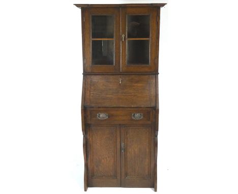 An oak Arts and Crafts bureau bookcase with shaped top over two glazed panel doors, the front with pigeon hole interiors over