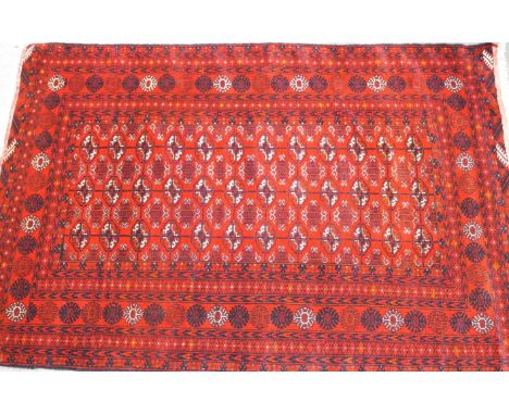 A hand knotted organic red dyed Bukhara rug, with a central panel of lozenge designs in a similar border, 185cm x 125cm