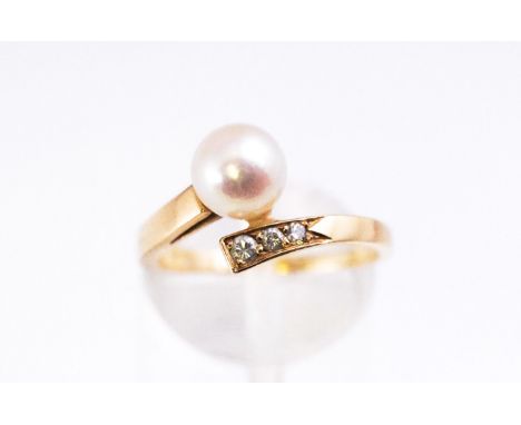 A yellow metal dress ring of crossover design set with a 7.0mm cultured pearl and three graduated round brilliant cut diamond