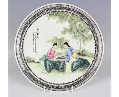 A Chinese famille rose porcelain plate, Republic period, painted with a scene of two seated maidens playing go at a rock tabl