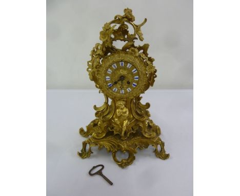A French gilded metal Rococo style mantle clock with enamel Roman numerals, two train movement to include key and pendulum