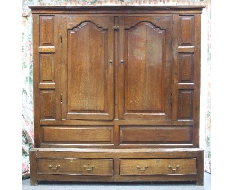 A mid 18th Century oak cupboard, the moulded cornice above two arched fielded panel doors above two drawers and surrounded by
