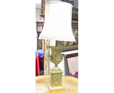 A campana shaped gilt metal urn lamp on a fluted socle and square base applied with floral scroll work, 48cm high