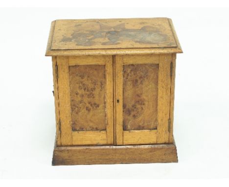 An Edwardian oak and pollard oak table cabinet, the top inlaid a star above twin panel doors enclosing pigeonholes and a draw