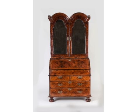A Queen Anne walnut double domed bureau bookcase with mirrored arched doors above a cross and feather banded fall concealing 