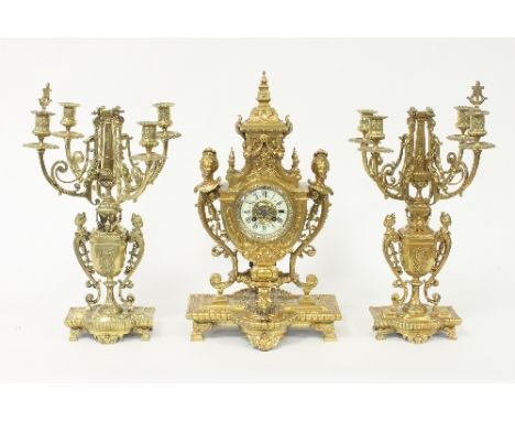 A late 19th Century gilt metal eight-day clock set, the clock with female mask head scrolls to the sides and fitted a cream c