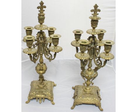 A pair of brass five-light candelabrum each with scrolling arms, mask mounted columns, on square bases with four splayed feet