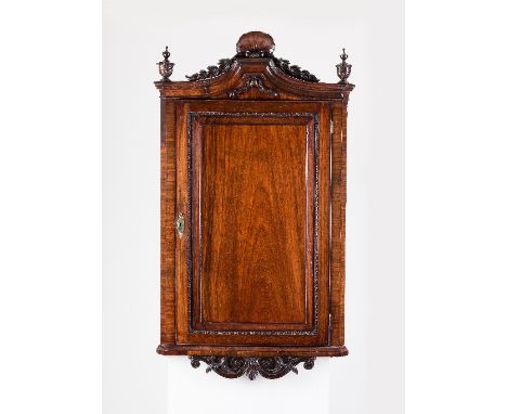 A George II padouk hanging corner cupboard, the shaped cornice carved with shell, husk and swags and with leaf carved finials