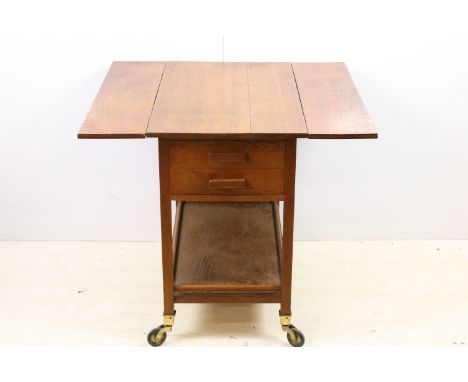 Stanley Webb Davies 1946 oak drop leaf table with side drawers and lower shelf set on castors, H 73cm, W 77cm, D 46cm (not ex