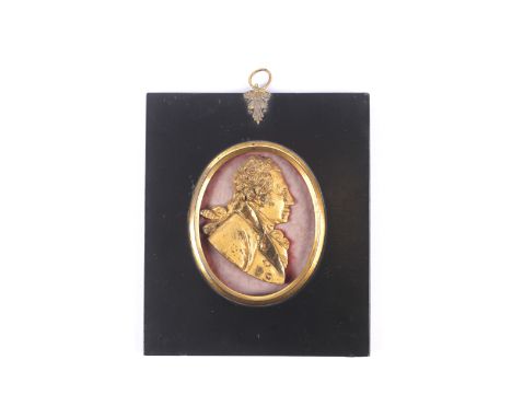 A gilt metal George III miniature profile portrait. Within an oval brass surround and in a japanned mount with a decorative b