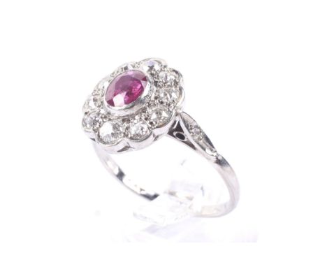 A mid 20th century platinum, ruby and diamond oval cluster ring. Rub-over set at the centre with an oval mixed-cut ruby withi