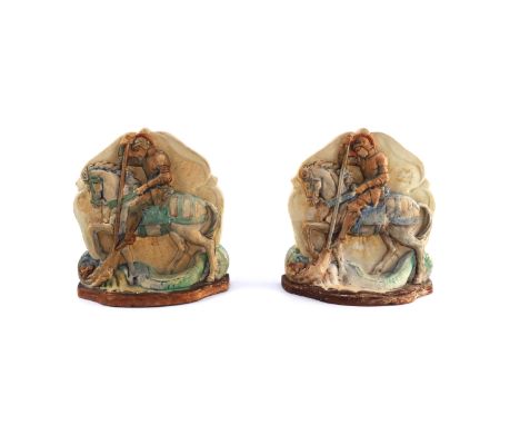 A pair of Compton Pottery bookends, moulded image of St George &amp; Dragon, pastel coloured on shield shaped backgrounds, fa