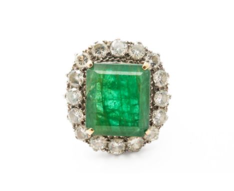 AN EMERALD AND DIAMOND CLUSTER RINGThe central claw set emerald cut emerald measuring 12.22mm x 10.79mm x 5.23 with an estima