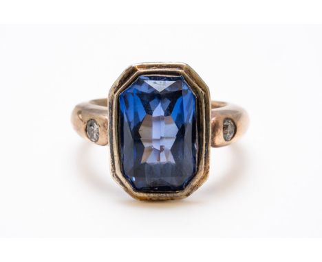 A SYNTHETIC SAPPHIRE AND DIAMOND THREE STONE RING (2)With a central bezel set mixed emerald cut synthetic sapphire measuring 