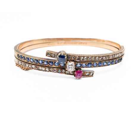 A SAPPHIRE, DIAMOND AND RUBY BANGLECentrally claw set with an oval cut sapphire, an old cut diamond and a oval cut ruby to a 
