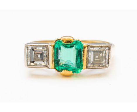 AN EMERALD AND DIAMOND THREE STONE RING (5)Mounted with a central emerald cut emerald, measuring approximately 6.4mm x 5mm an