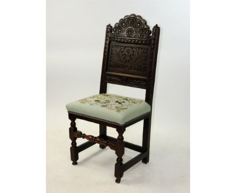 A carved oak backstool 17th century and later with lunette carved cresting and flower head centred scroll top rail above a le