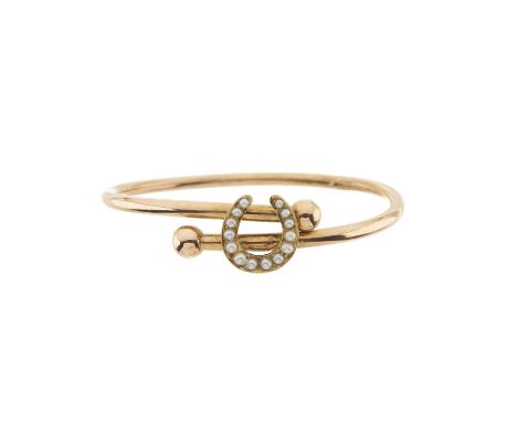 A late 19th century gold bangle bracelet, with split pearl horseshoe overlay and bead terminals, inner diameter 5.8cm, 9gOver
