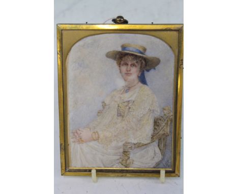 AN EDWARDIAN WATERCOLOUR MINIATURE PORTRAIT OF A SEATED YOUNG LADY WEARING A WHITE DRESS AND SUN BONNET, INITIALLED E.G.K.