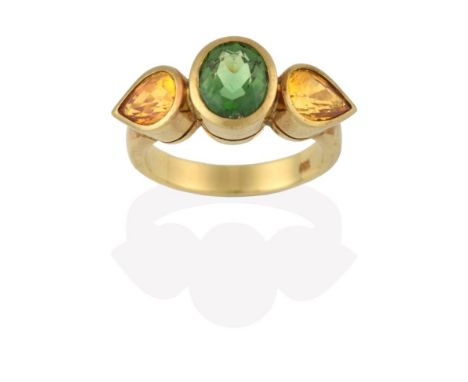 A Green Tourmaline and Yellow Sapphire Three Stone Ring, the central oval cut green tourmaline flanked by pear cut yellow sap