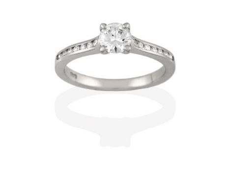 A Platinum Diamond Solitaire Ring, the round brilliant cut diamond in a claw setting, to a channel set diamond shoulder plain