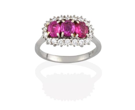 A Ruby and Diamond Cluster Ring, three oval cut rubies within a border of round brilliant cut diamonds, in white claw setting