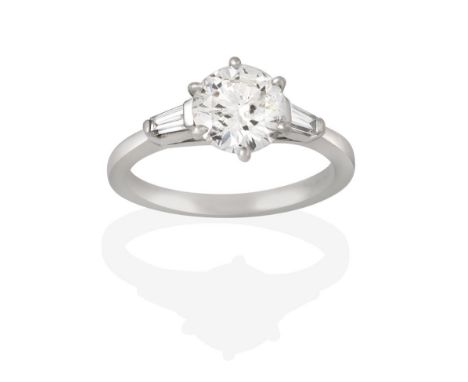 A Platinum Diamond Solitaire Ring, the round brilliant cut diamond in a claw setting, to a tapered baguette cut diamond set s