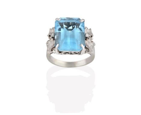 A Blue Topaz Ring, the emerald-cut blue topaz in a white four claw setting, to textured foliate shoulders inset with eight-cu