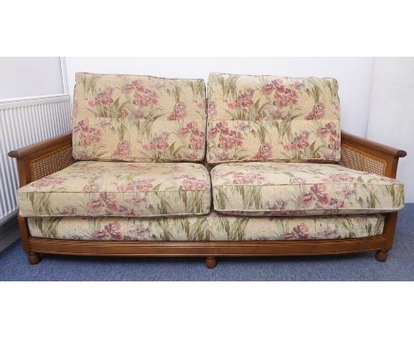 A good Ercol two-seater sofa; rich coloured elm and rattan-caned sides; upholstered lily pattern cushions (virtually as new c