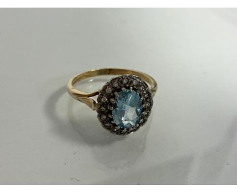 A 9ct yellow and white gold ring set with a central oval blue topaz surrounded by halo of Round cut diamonds. Blue topaz 1.10