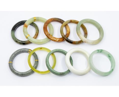 A collection of ten jade/ hardstone bangles in varying shapes and sizes and colours including grey, brown, green, white etc, 