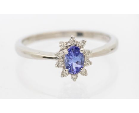 A tanzanite and diamond platinum set cluster ring. comprising an oval mixed cut tanzanite approx 5 x 3mm, within a border of 