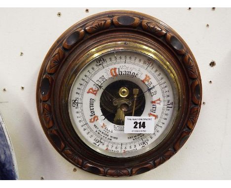 A wall mounted aneroid barometer, oak cased with decorative carving, white enamelled dial with open centre displaying the mom
