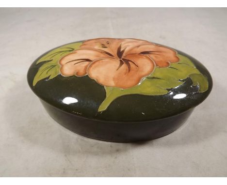 Moorcroft Pottery - An oval lidded trinket box decorated with pink coral hibiscus on a green ground, 4cm (h) x 13cm (w) x 8.5