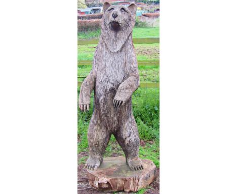 A weathered forest art chainsaw carving of a standing bear with nicely defined features carved from a single tree trunk appro