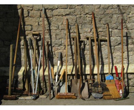 A galvanised dustbin containing a collection of wooden long handled gardening tools, some with T shaped handles 