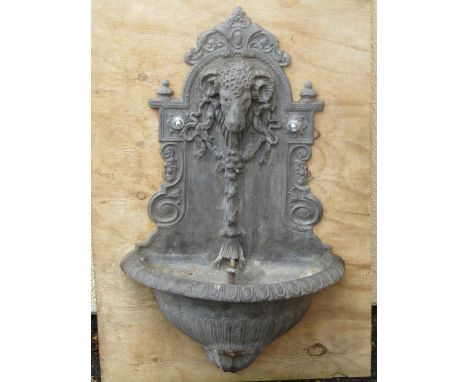 An old lead garden wall fountain with rams head mask and decorative trailing tied ribbon and further classical detail over a 