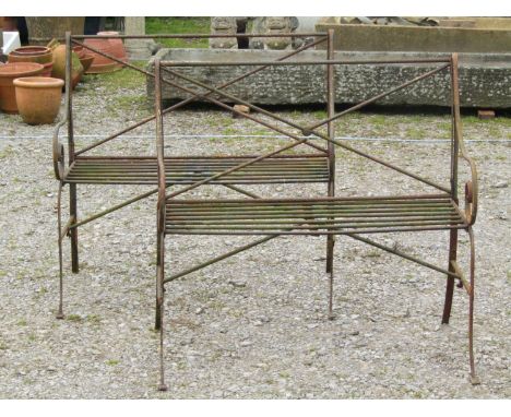 A pair of weathered light steel regency style two seat garden benches with open scrolled arms, open X framed backs and swept 