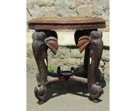 An Indian hardwood occasional table of circular form with repeating geometric detail raised on four elephant head trunk suppo