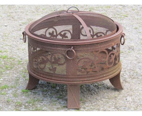 A weathered light steel/aluminium garden brazier/firepit of squat cylindrical form with loose domed cover and repeating scrol