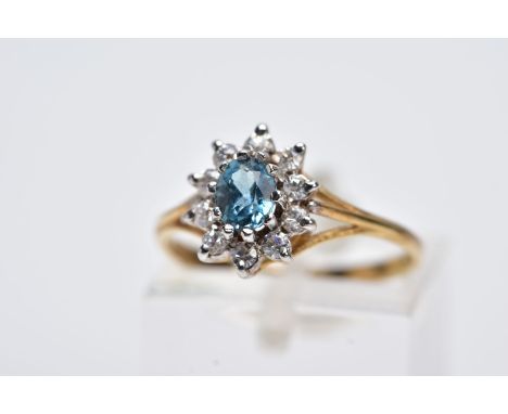A YELLOW METAL CLUSTER RING, designed with a central oval cut blue topaz, within a circular cut colourless paste surround, tr