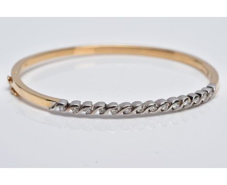 A YELLOW METAL DIAMOND BANGLE, the hinged bangle designed with a row of crossover mounted round brilliant cut diamonds, total