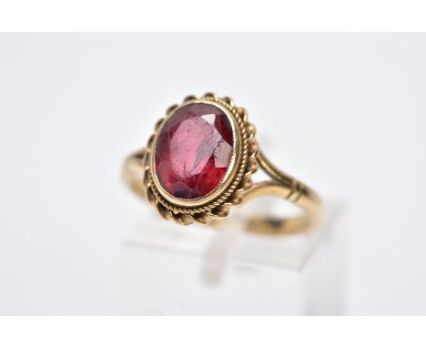 A 9CT GOLD GEMSET RING, designed with an oval red stone assessed as tourmaline, within a collet  mount and rope twist surroun