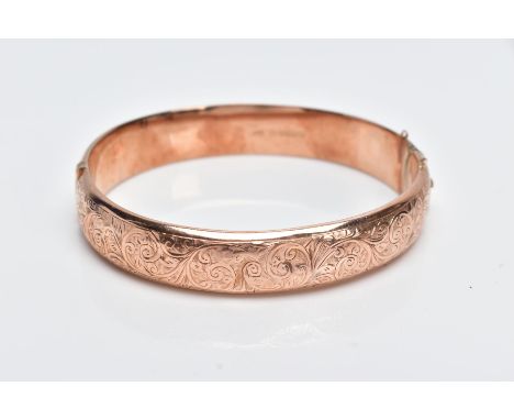A 9CT ROSE GOLD BANGLE, hollow hinged bangle with a decorative foliate engraved design to the one side, fitted with an integr